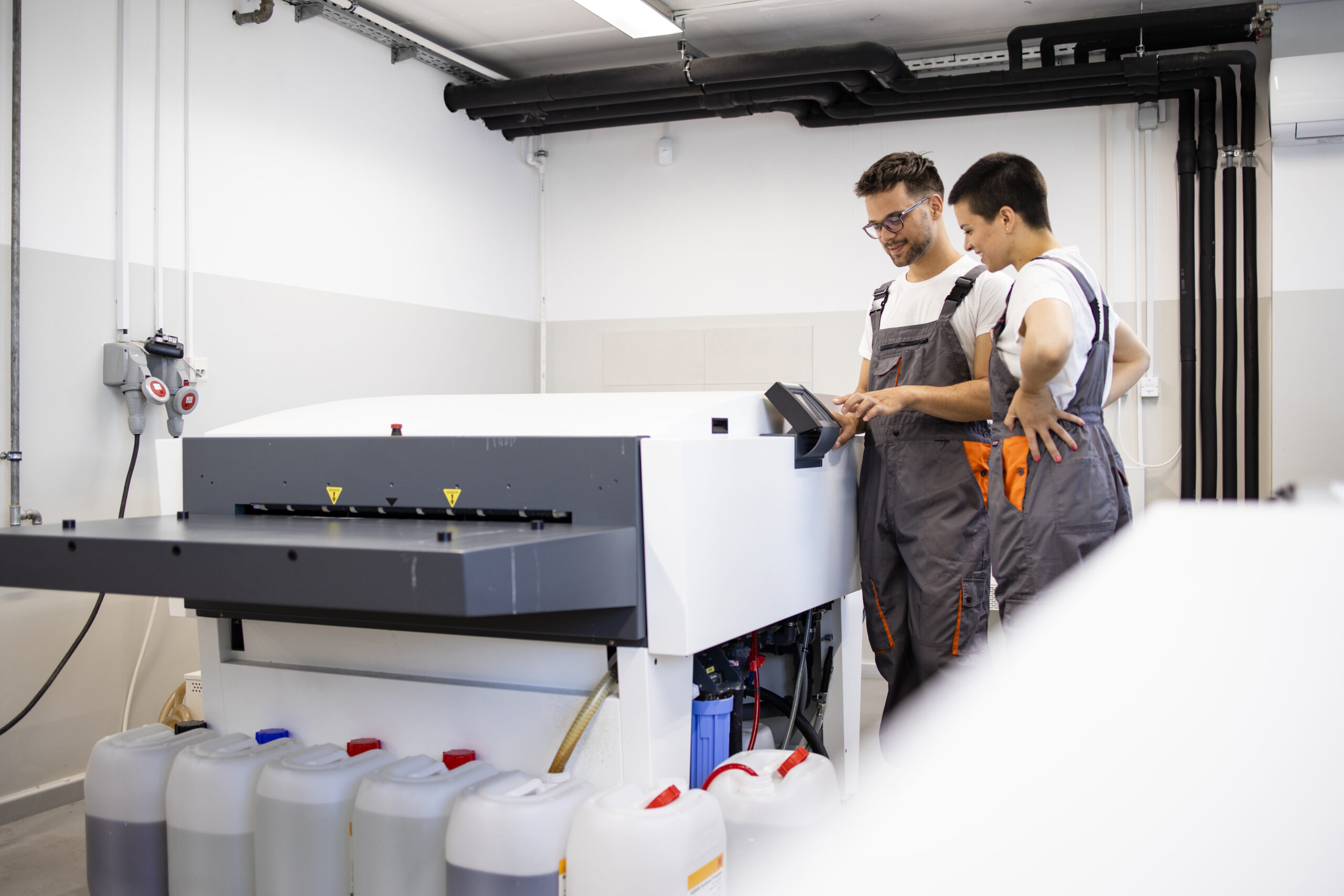 Print workers operating computer to plate machine in print shop.