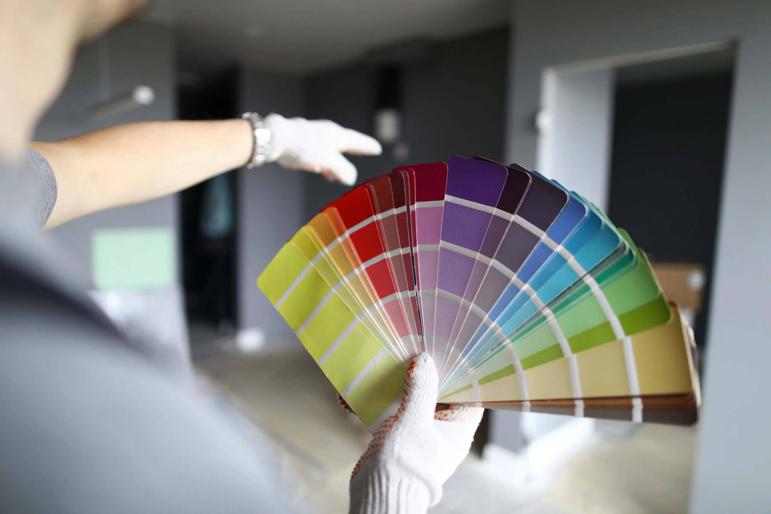 Repairman in gloves standing in flat, looking at walls and palette and trying to choose color for interior details. Professional repairman during work concept