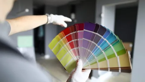Repairman in gloves standing in flat, looking at walls and palette and trying to choose color for interior details. Professional repairman during work concept
